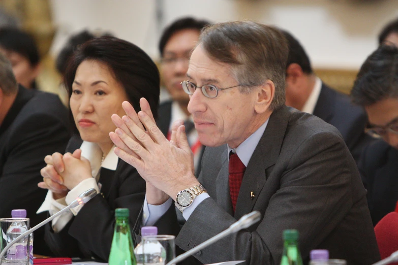 a number of people at a meeting with one man on his phone