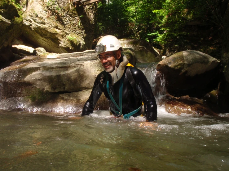 the man wearing a wetsuit is wading through a stream