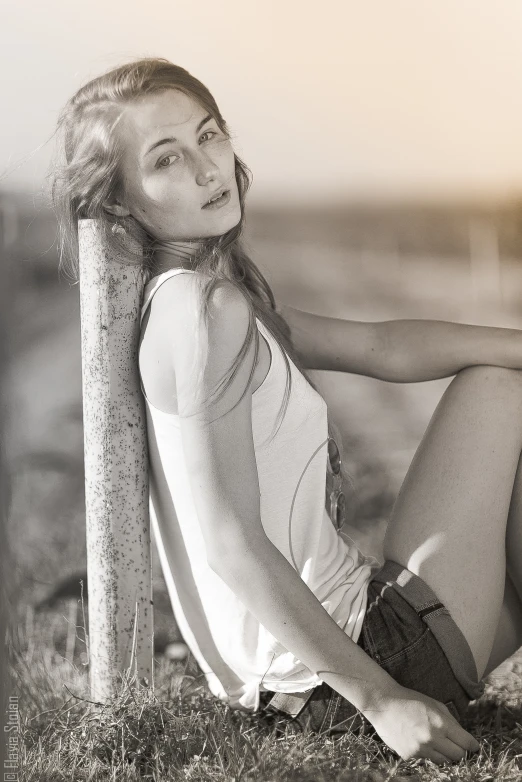 a woman is sitting by a pole in the grass