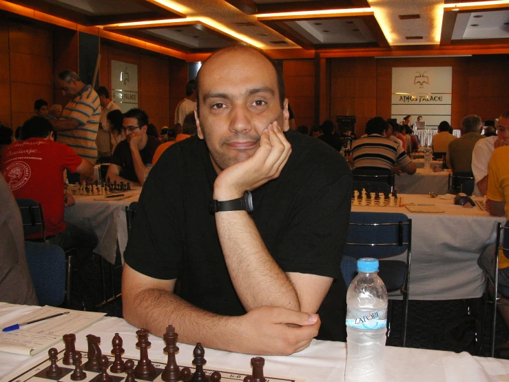 a man sitting at a chess table with people sitting at the tables