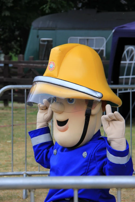 a man in a blue jacket wears a yellow hardhat while talking on a cell phone