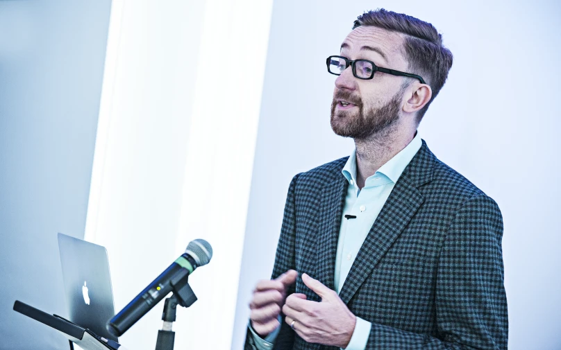 man with black glasses talking in front of microphone