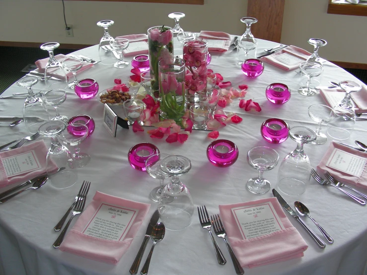 the white table is set with pink napkins, place mats and silverware