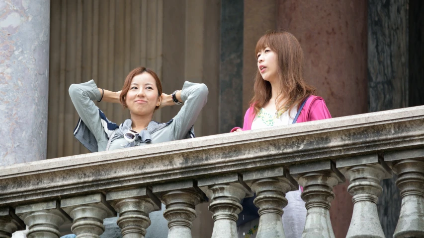 two women are standing by the balcony, looking at soing