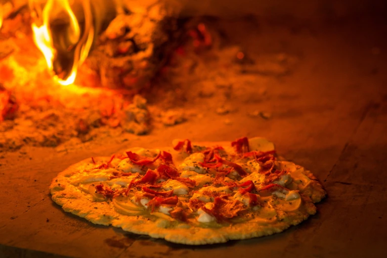 two personal pizzas sitting next to an oven that has fire in it