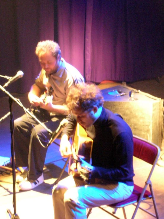 two men sitting down in chairs with an instrument