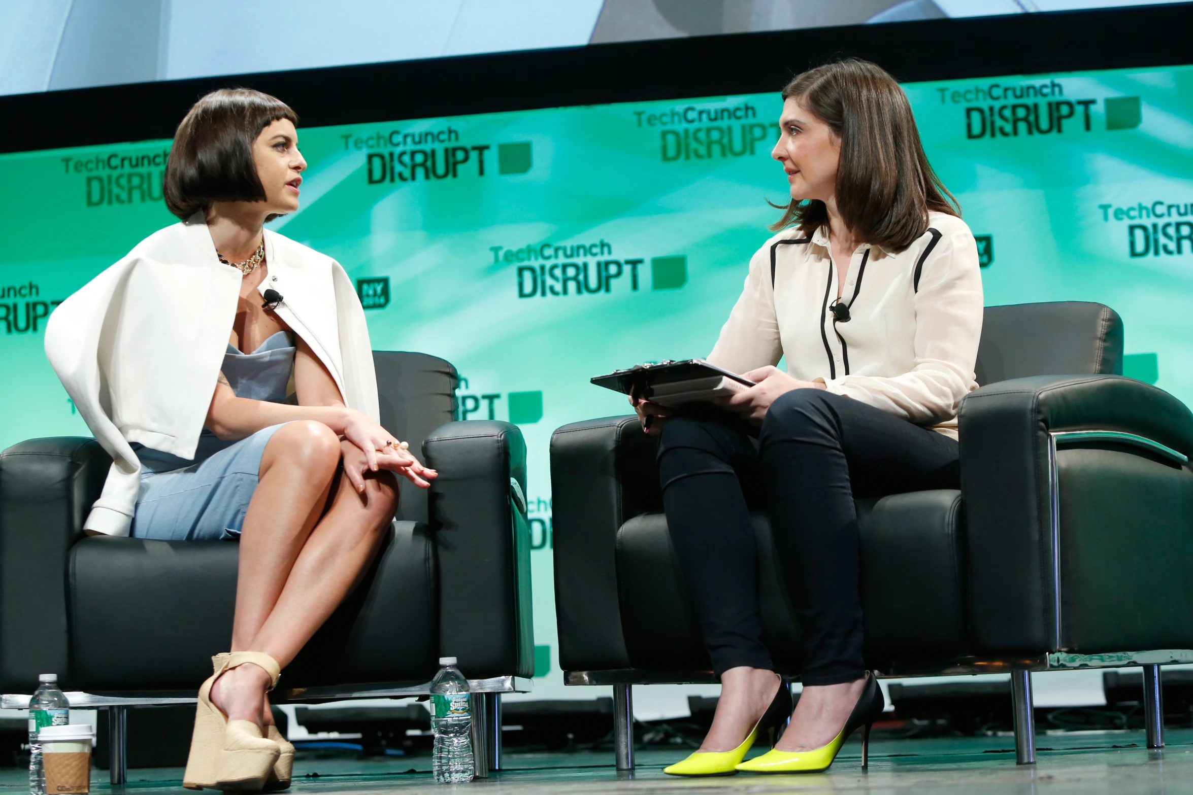 two women sitting on black chairs in front of a green backdrop