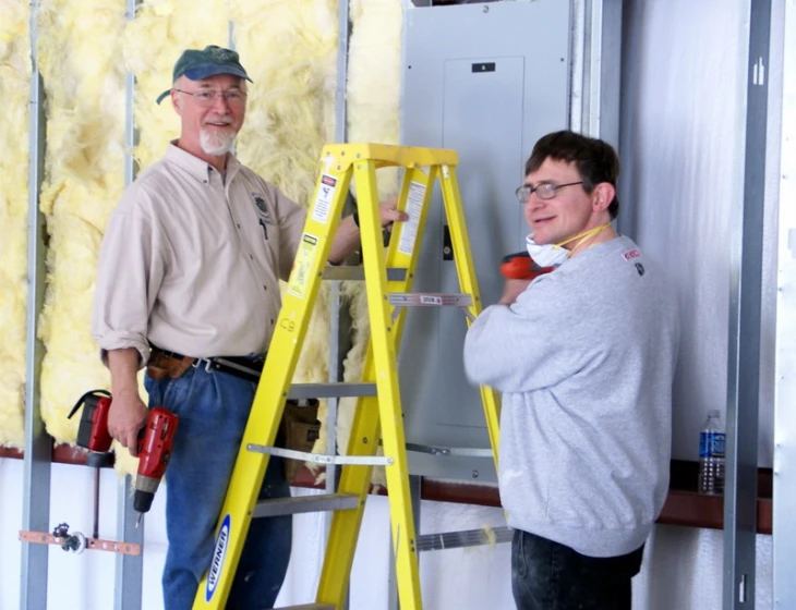 two men standing together in a building and one has a drill tool on his hand