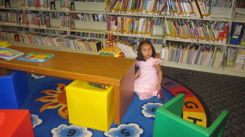 a little girl is standing next to a desk in a book store