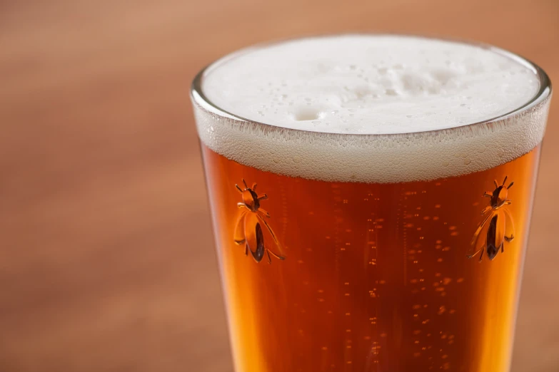 a glass filled with white beer sitting on top of a wooden table