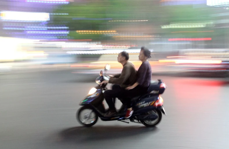 two people on a scooter are driving down the road