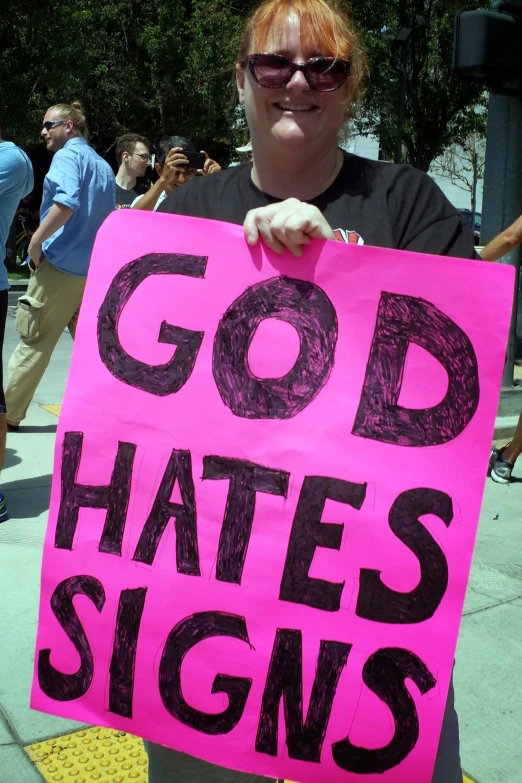 a woman holding up a pink sign that says god hates signs