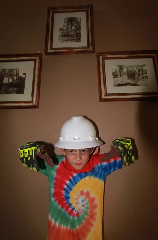 a boy in a hard hat and shirt holding his arms up