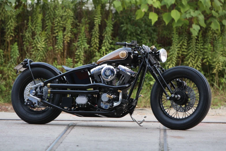 a black motorbike with a chrome plated frame is parked next to some greenery