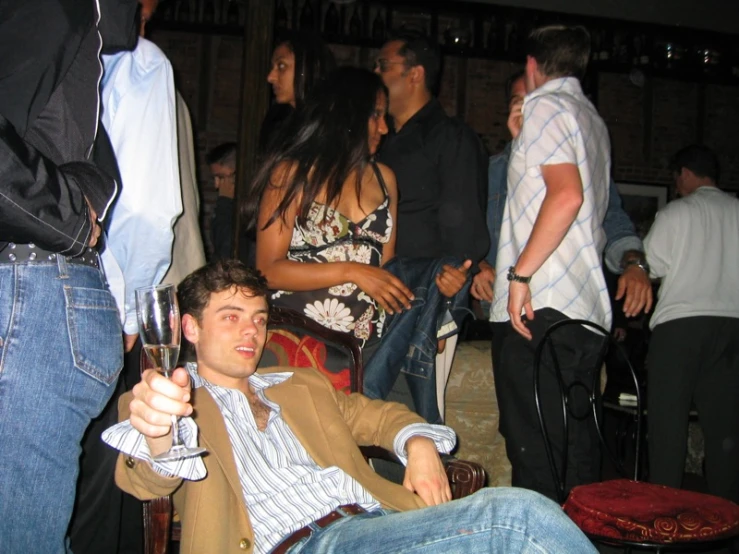 a young man sitting in a chair with his foot propped up and arms crossed and drinking wine