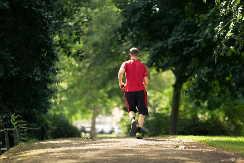 man wearing red shirt and black shorts running on tree lined road