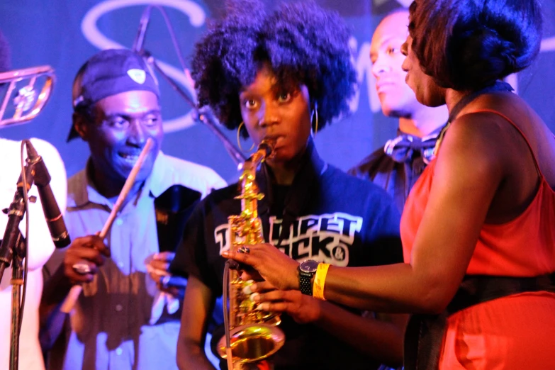 woman holding up saxophone with group of musicians behind her