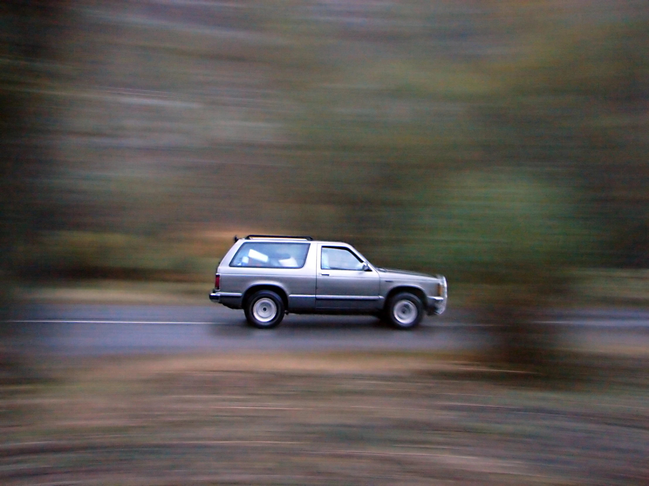 an old silver truck traveling past a forest