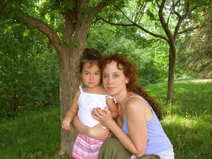 two women holding a baby while sitting underneath a tree