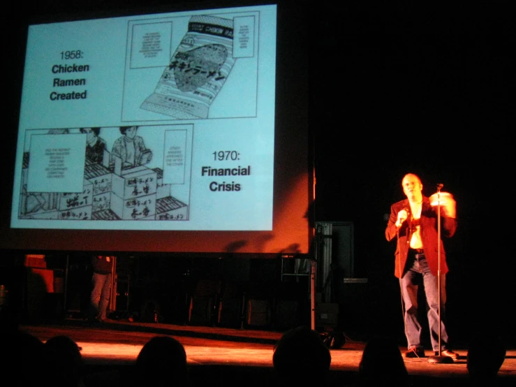 a man standing on a stage, speaking into microphone