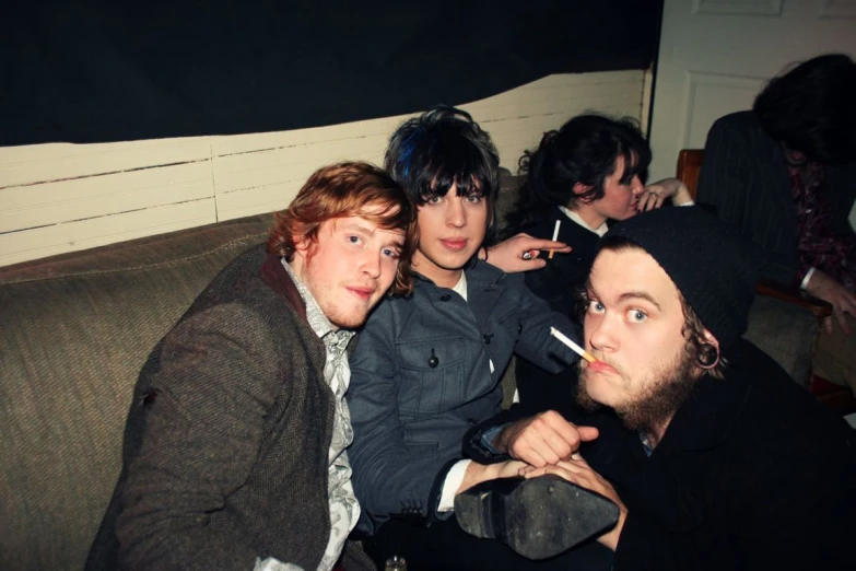 the three men are sitting on a couch smoking