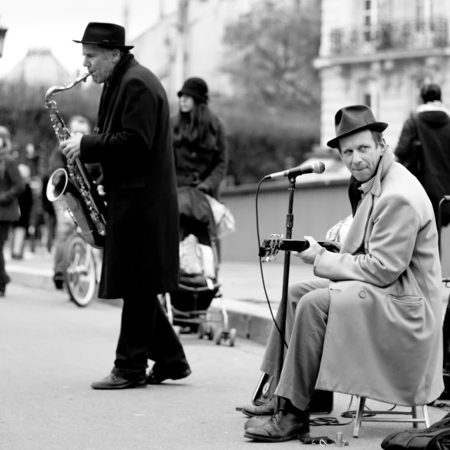 a man with a hat and coat plays saxophone while another man is on a bike