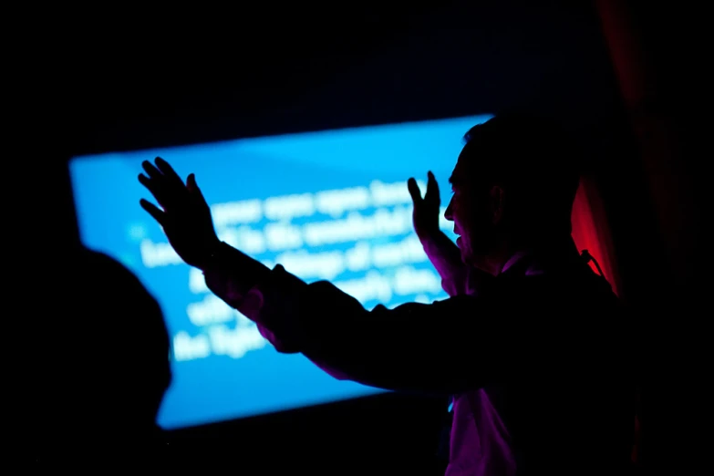 silhouette of a man raising his hands at a dark background