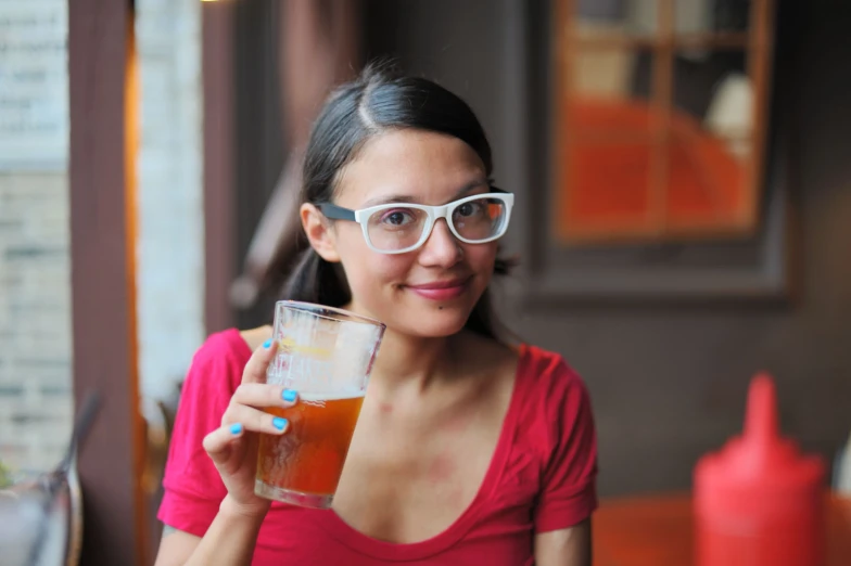 a woman in glasses holds up a glass with some drink inside it