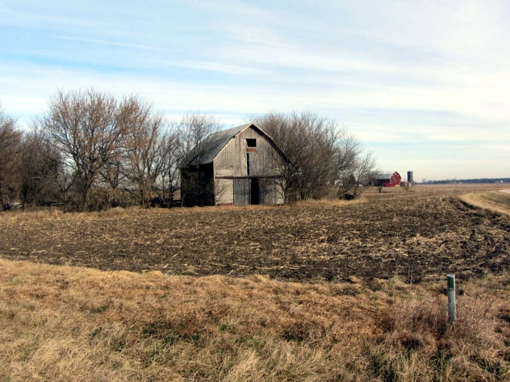 an old barn with a plowed field in the foreground