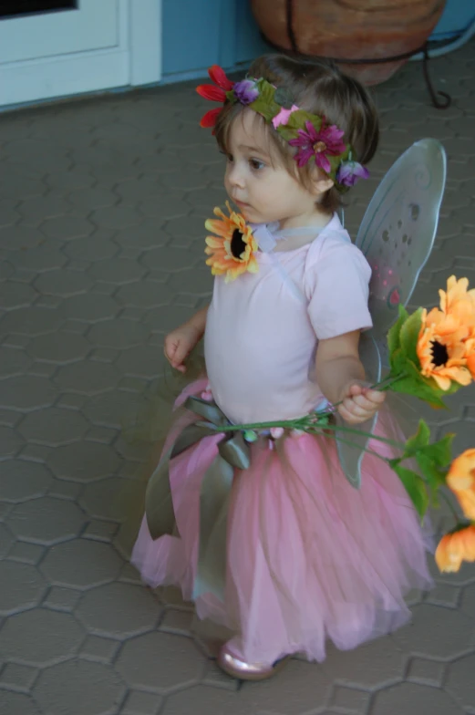 a small girl dressed in fairy clothes and holding an orange flower