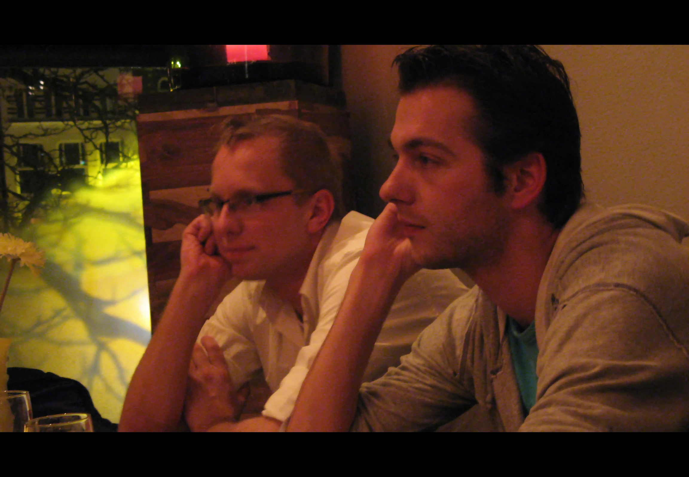 two men sitting next to each other in front of a vase with flowers on it