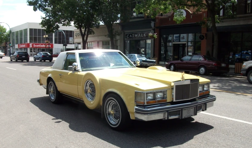 a yellow, classic - looking car is driving down the street