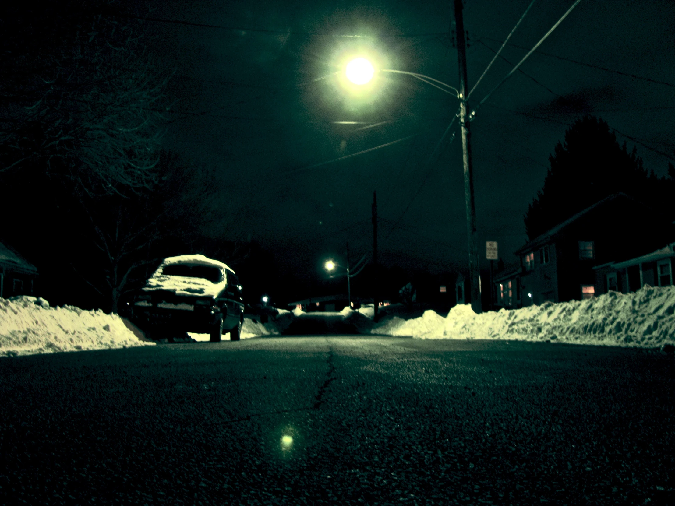 a night time image of a snowy street with a car parked on the side