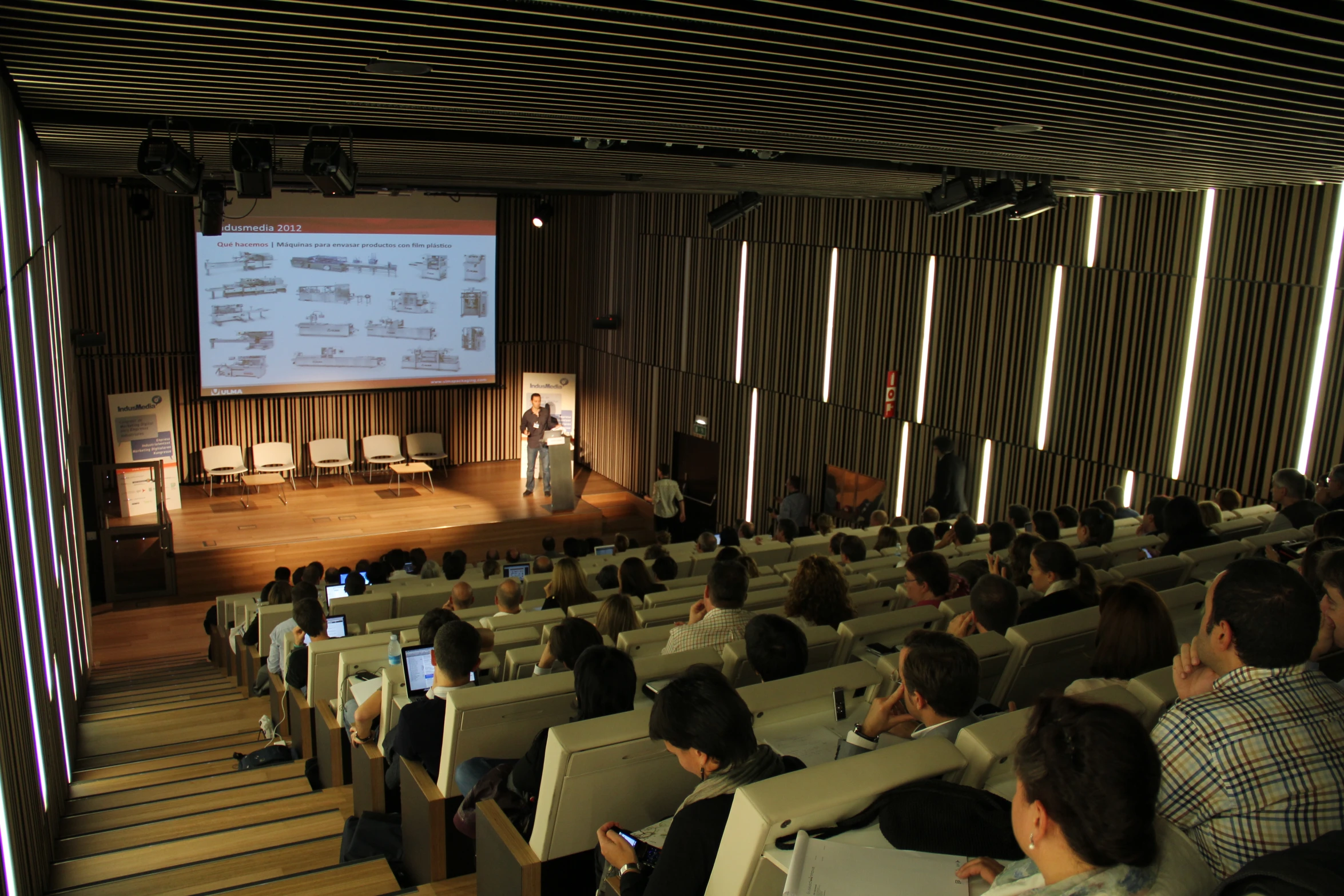 people watch a presenter in front of a large audience