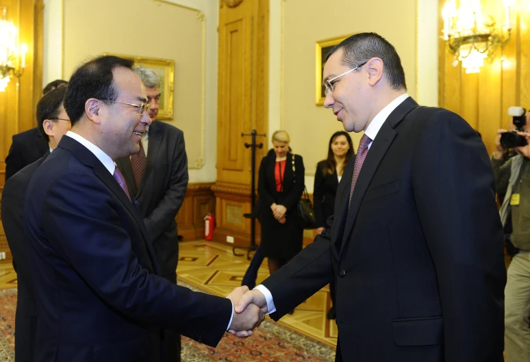 two men shaking hands with other people in suits behind them