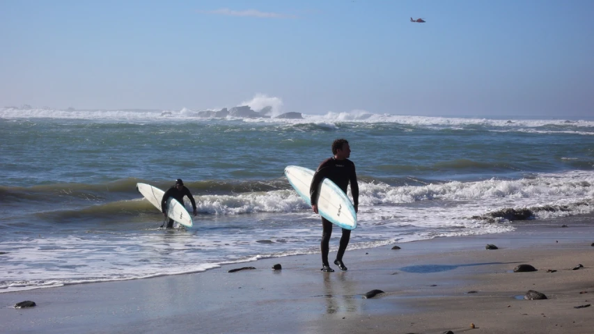 the two surfers are walking out into the water on the beach