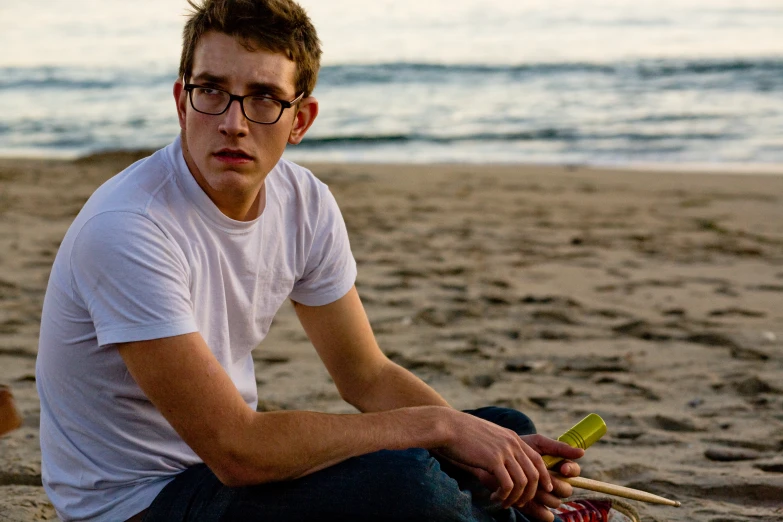 a man in glasses sitting on the sand