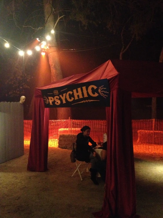 a man sits in a small tent with a psychic sign above it