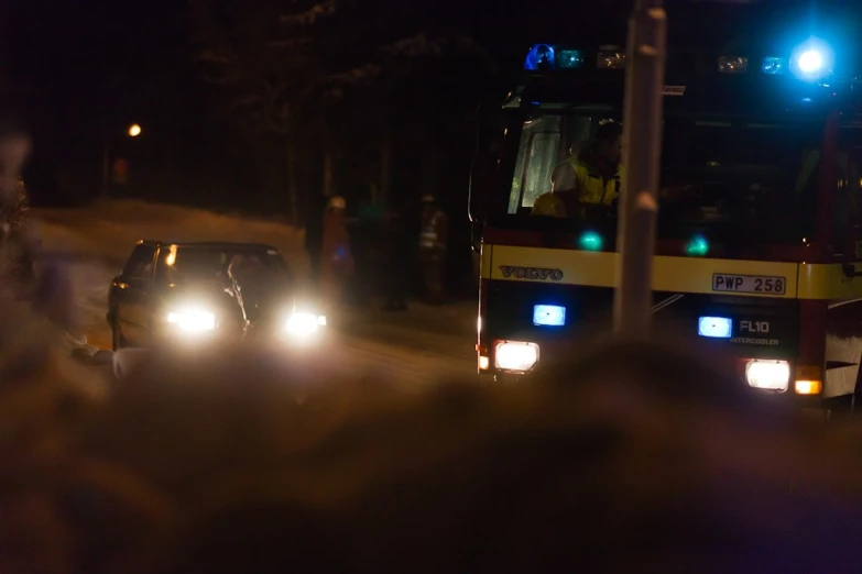 some buses on a street at night with people watching