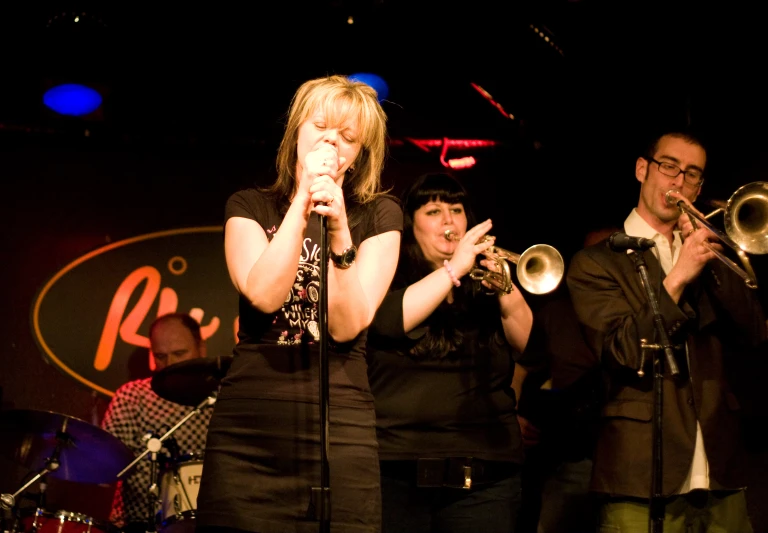 a woman standing in front of two trumpet players