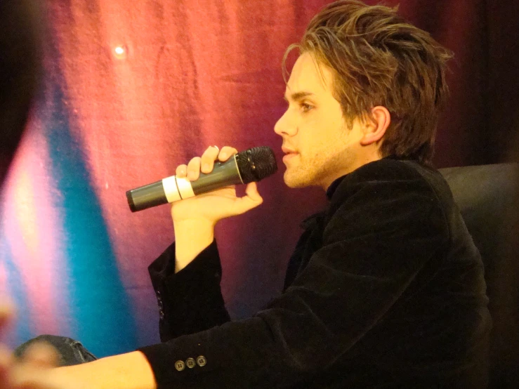 a man sitting down holding a microphone while wearing a black shirt