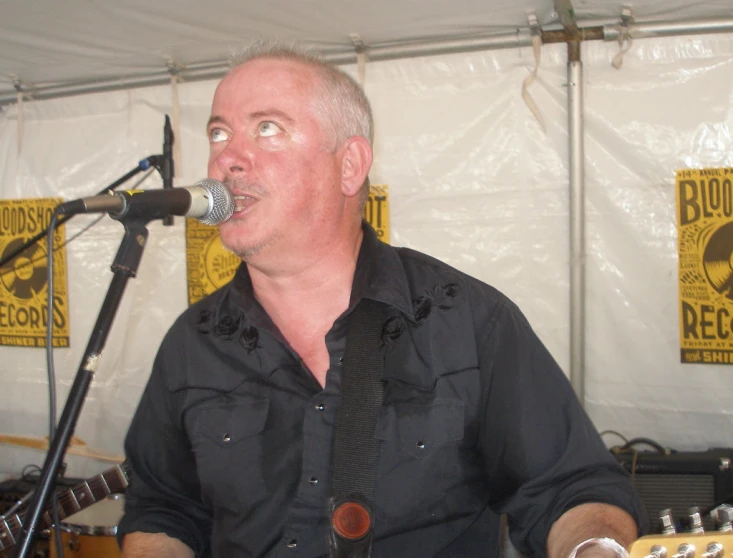 an older man in front of a microphone with a guitar