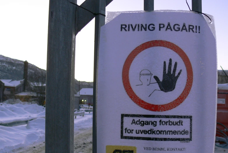 a sign posted next to a fence with snowy countryside