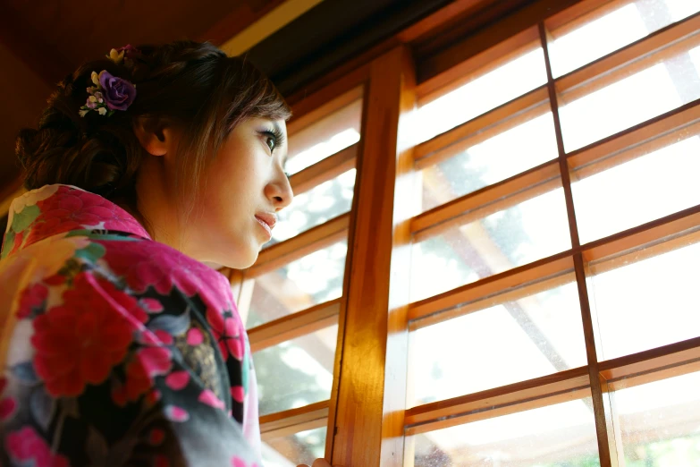 a woman looking out a window with bright blinds