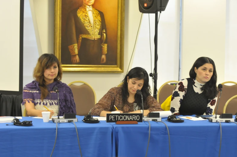 three woman sit at a table in front of a large painting