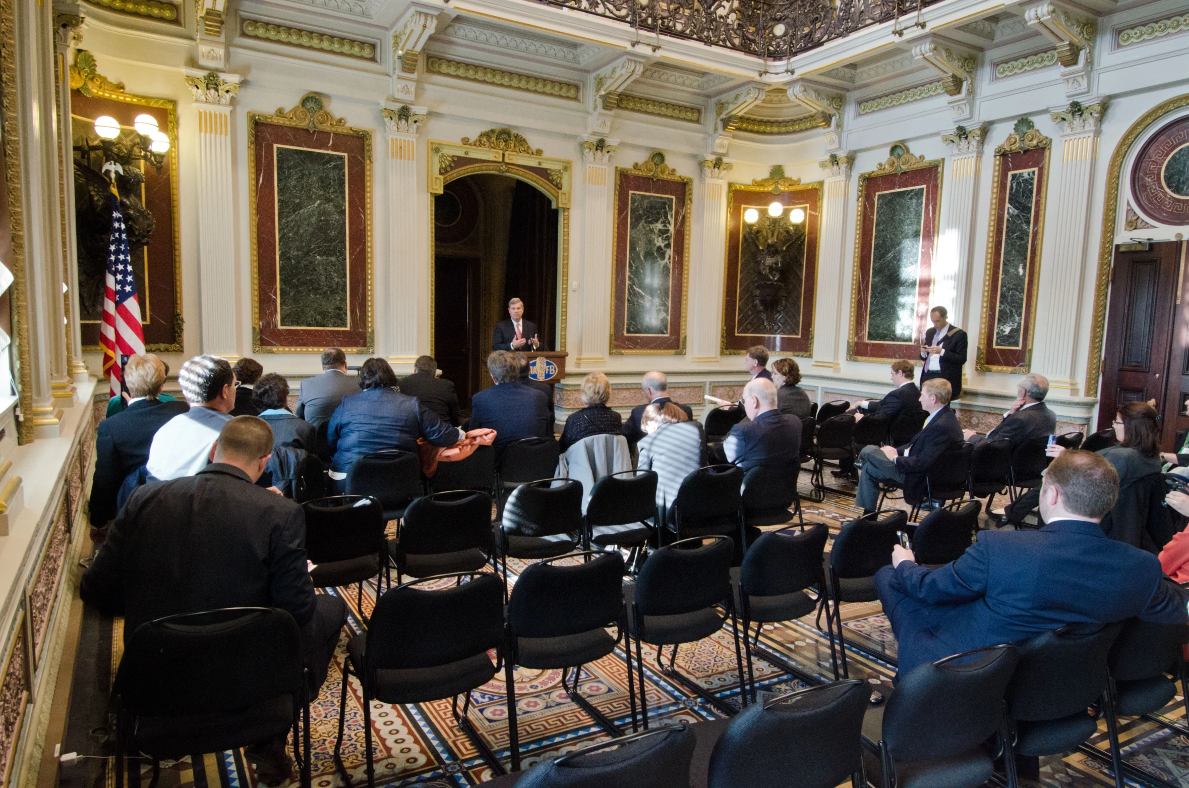 several people sit in chairs in the middle of an ornate room