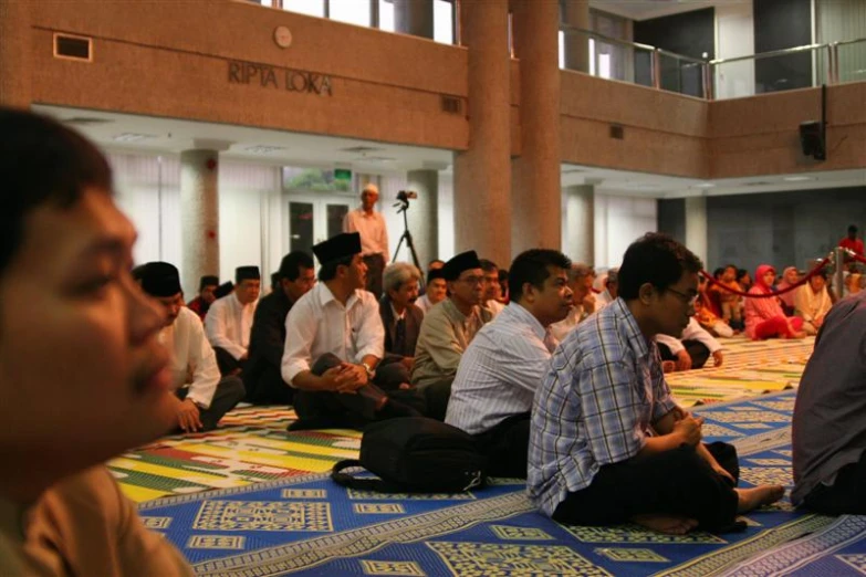 several men sitting in a room and a person standing up in front of the room