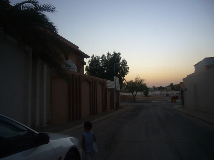 a little boy walking on a street near a car