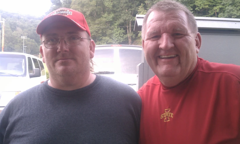 two men posing for the camera while standing in front of a parking lot