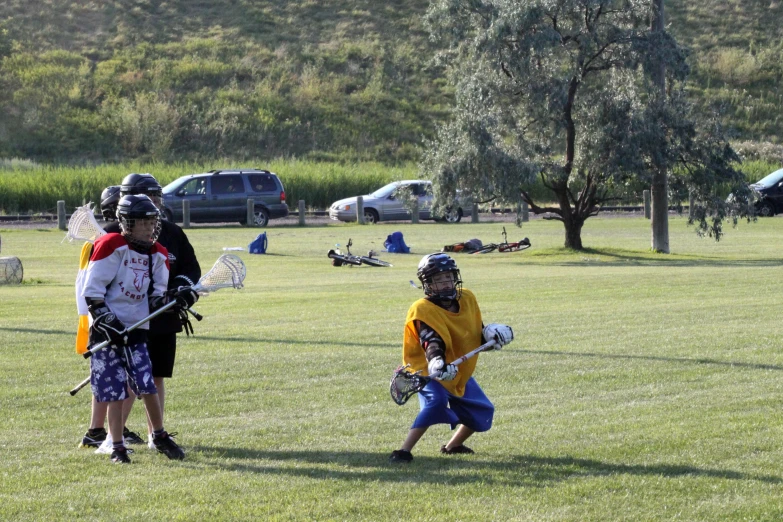 people playing with lacrosse in a field with trees and vehicles behind them